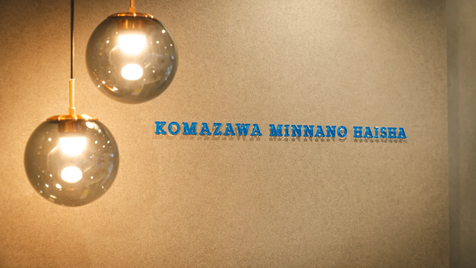 落ち着いた壁面に「KOMAZAWA MINNANO HAISHA」の青い立体文字と、2つの球形ペンダントライトが照らす歯科医院の内装写真